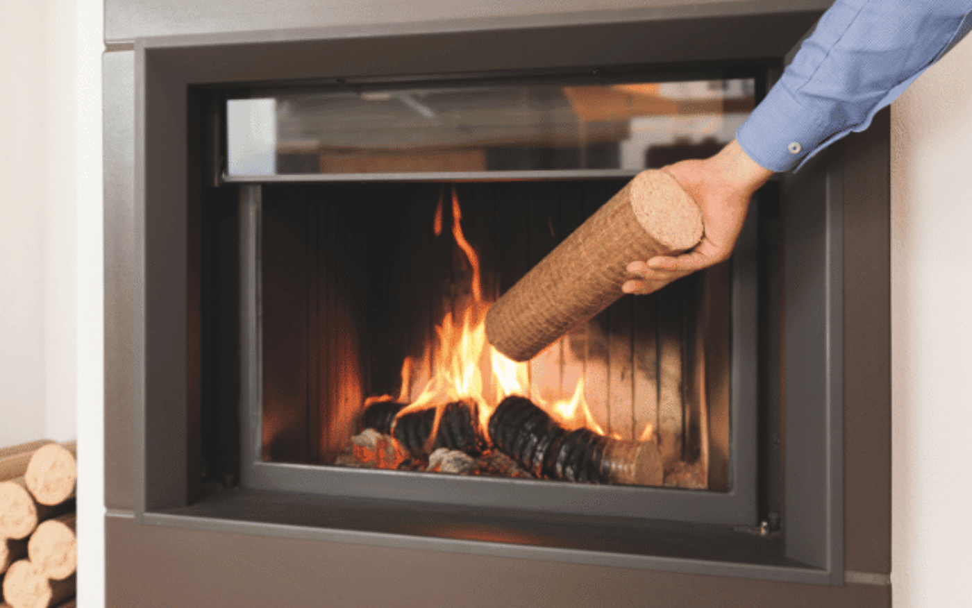 Holzbriketts Vorteile im Überblick! Person legt Holzbrikett in modernen Kaminofen mit brennendem Feuer.